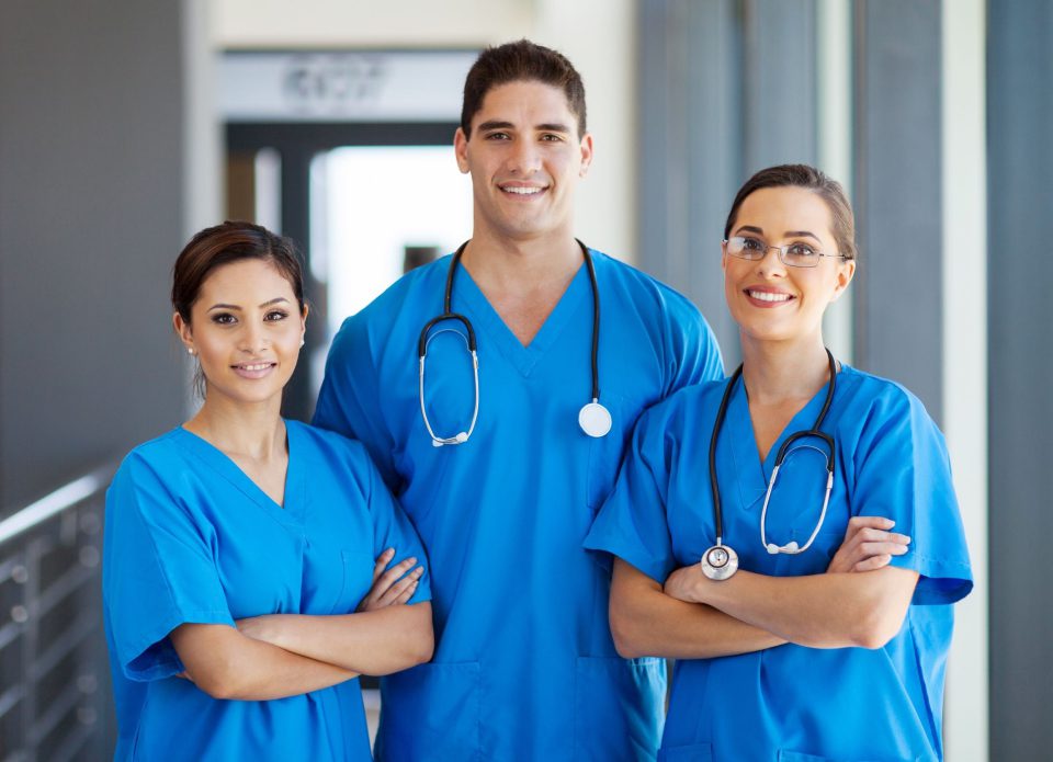 Three nurses in blue scrubs are posing for a picture.